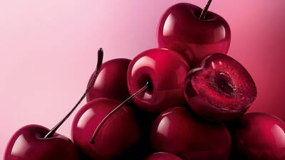 Un monton de cerezas brillantes, de color rojo oscuro a negro, llenan la parte inferior y derecha del encuadre, sobre un suave fondo rosa.