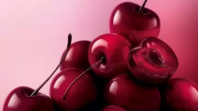 Un monton de cerezas brillantes, de color rojo oscuro a negro, llenan la parte inferior y derecha del encuadre, sobre un suave fondo rosa.