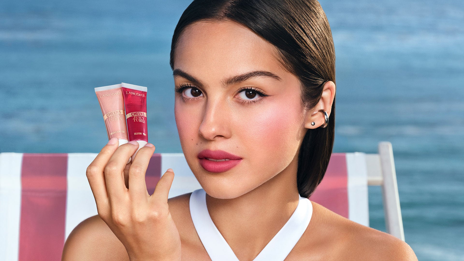 Modelo sosteniendo dos Juicy Tubes de Lancôme junto al mar.